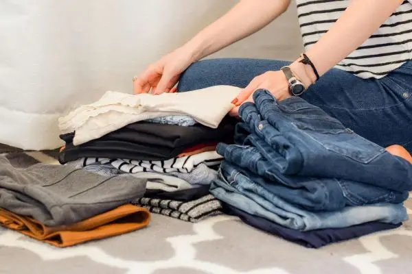 A person sorting and folding clothes into neat piles on the floor, showing a decluttering and organization process.
